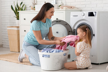 Young woman and her little daughter doing laundry at home