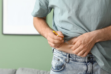 Diabetic young man giving himself insulin injection at home, closeup
