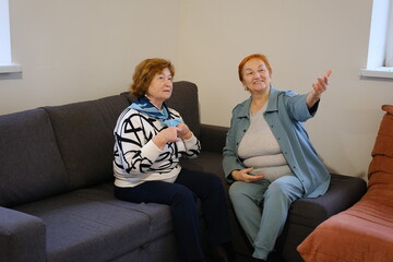 two Older 70s Hispanic woman lead pleasant, trustworthy conversation seated on sofa at home....
