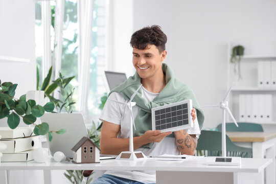Male engineer with portable solar panel and wind turbine models video chatting at table in office - Powered by Adobe