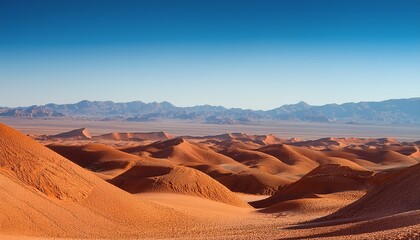 Vast Desert Landscape With Layered Red Ochre Hills And Distant Blue Mountains Under Clear Sky