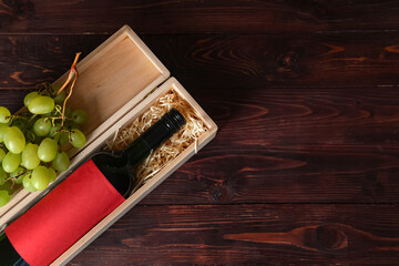 Box with bottle of wine and grapes on wooden background