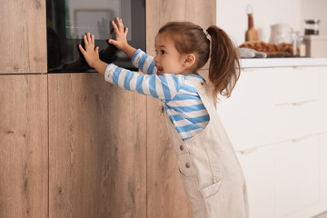 Cute little girl near electric oven in kitchen. Child at risk