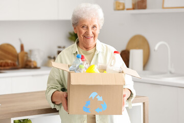 Senior woman with box of garbage in kitchen. Waste sorting concept