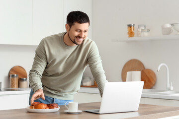 Young male teacher with laptop and pastry giving online lesson at home