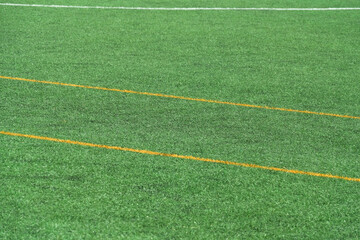 Obraz premium Green synthetic grass, artificial turf sports field with yellow and white lines.