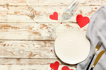 Table setting for Valentine's Day with red paper hearts and glass on white wooden background