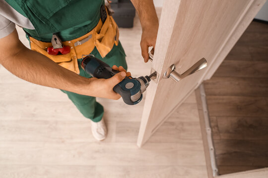 Male worker with electric drill repairing door at home, closeup