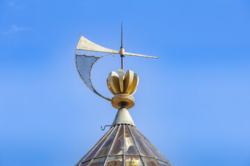 Close-up of the golden, gilded cockerel wind vane, also known as a weathercock, perched atop the spire of the Riga Cathedral (Dome Cathedral) against a clear blue sky. © erikzunec