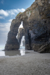 Rock arches and towering cliffs at As Catedrais Beach in Ribadeo, Spain, captured at low tide with soft light, ocean waves, and dramatic natural formations