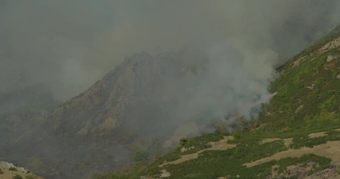 Large amount of white smoke consuming rocky mountain - low, still shot