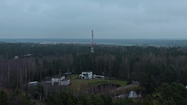 Aerial perspective showcases lone radio mast amidst thick forest under stormy sky conditions