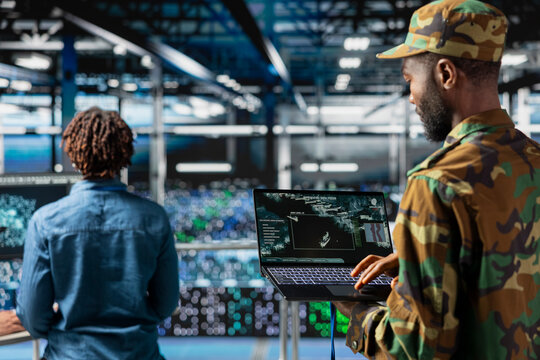 African american army soldier in command center server room using AI tools on laptop, detecting cyber threats and ensuring national safety. Military data center expert use detection software.