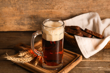 Mug of fresh kvass with slices of bread and wheat on wooden background