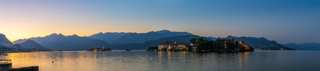 Obraz premium View of Isola Bella at twilight, highlighting the Borromeo Palace on the left and the elaborate terraced gardens on the right, with the Alps silhouetted against the morning sky