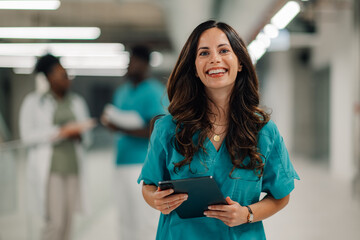 Smiling medical professional holding tablet standing in hospital corridor