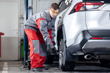 Young male auto mechanic working on car in garage service center for replacement of winter tires