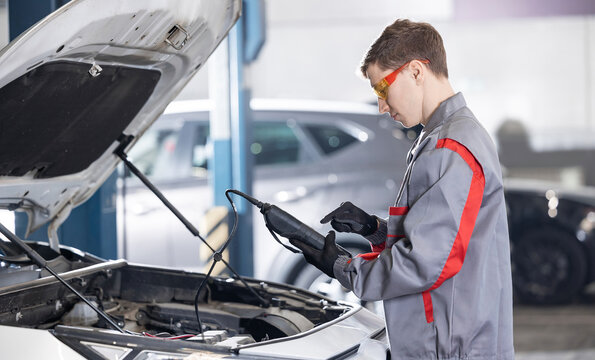 Caucasian male mechanic using diagnostic tool for battery level on car engine in garage