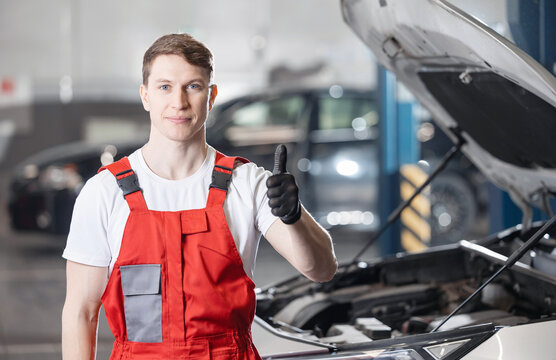 Cheerful man mechanic in overalls smiles confidently, giving thumbs up in workshop, car repairs service