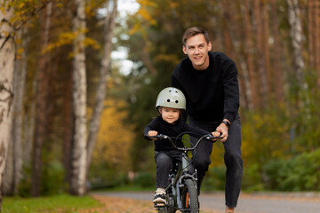 Father teaching young daughter girl to ride bicycle in autumn forest setting