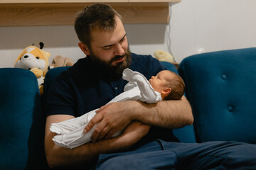 Caucasian male adult holding newborn baby on sofa, Lifestyle moment of paternity.