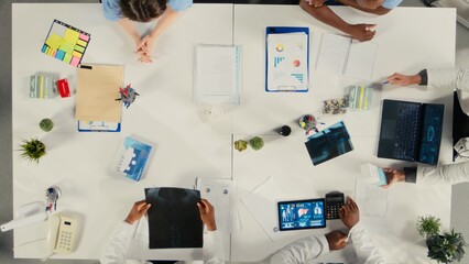Top down view of doctors and nurses in meeting discuss treatment strategies and diagnosis plans. Diverse healthcare team collaborates on innovation and patient care solutions.