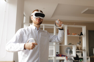 Young caucasian male using vr headset with controllers in modern room developer office