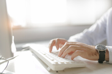 Close-up of caucasian male adult using computer keyboard in sunlit office