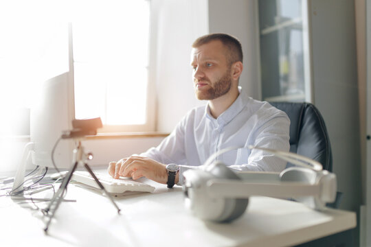 Owner business young caucasian male working on computer in modern office setting with vr headset nearby - Powered by Adobe