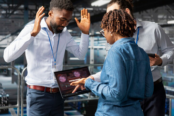Engineers team in server farm stressed by critical error alert on laptop during diagnostics session on industrial platform. Anxious staff troubleshooting system fault affecting performance.