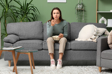 Obraz premium Upset young woman with popcorn watching movie on sofa at home