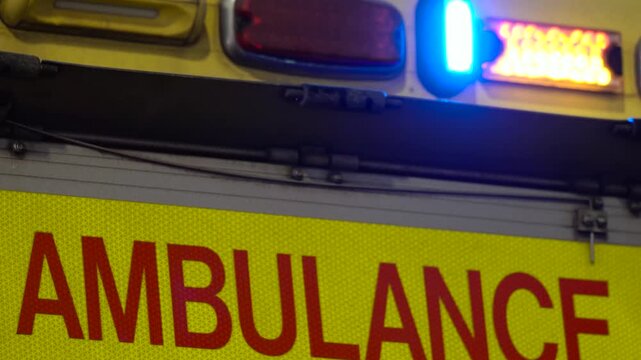 Ambulance Emergency Service Vehicle Rear View Strobe Lights Flashing Red, Blue At Night, Lettering Text Sign, High-Visibility Battenburg Pattern Livery, London, United Kingdom