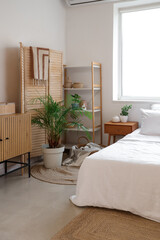 Chest of drawers, cozy bed with bedside table, shelving unit and folding screen in interior of bedroom