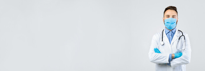 A man dressed in a white coat stands confidently with his arms crossed. He wears a blue mask and...