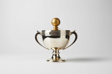 A gleaming silver trophy cup with a decorative lid and handles, featuring a unique golden tennis ball finial, against a clean white background.