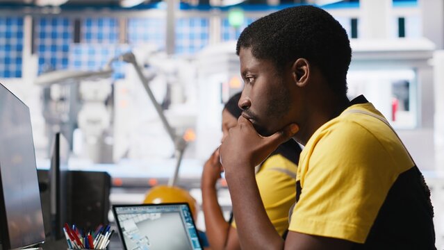 Male specialist adjusts machine parameters for solar panel production, working at a high tech manufacturing plant. Black engineer analyzing technical data on a computer. Camera A.