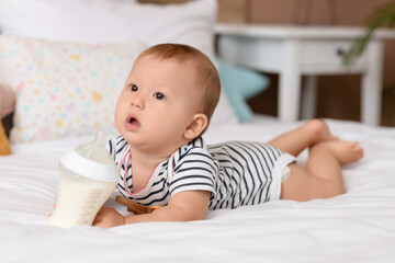 Cute baby with bottle of milk lying in bedroom