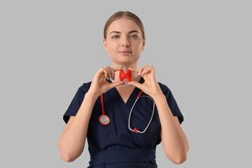 Female endocrinologist with thyroid gland model on grey background