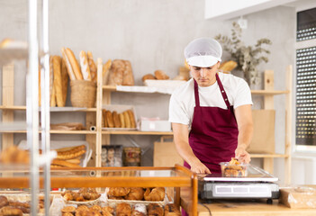 Young baker weighs fresh croissants on a scale and places them in a plastic container