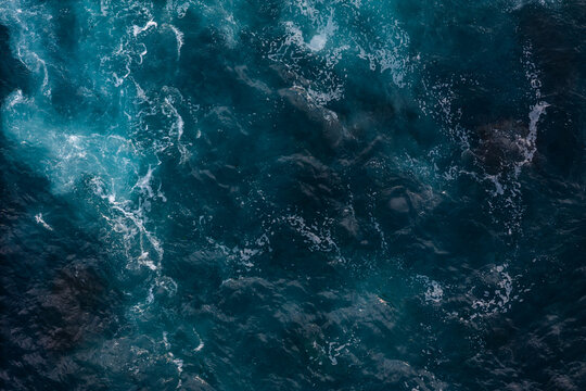 Ocean surface with white foam and dark lava reefs, aerial top down shot