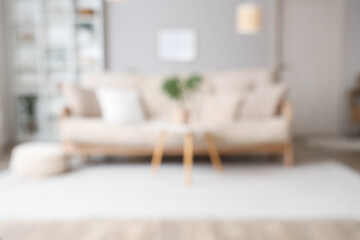 Blurred view of light living room with beige sofa, table and shelf unit