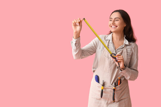 Young female construction worker with tools and measuring tape on pink background. Woman in male profession concept