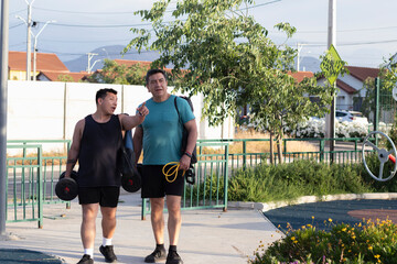 dos hombres con ropa deportiva caminan por un parque buscando un lugar para hacer ejercicio