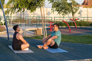 dos hombres con ropa deportiva practican meditaci&oacute;n en un parque, al aire libre sentados sobre un matt de yoga
