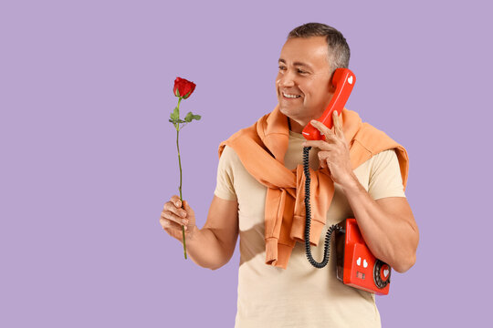 Happy mature man with rose flower and retro phone on purple background. Valentine's day celebration