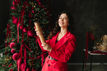 Fototapeta premium Smiling girl pops party popper near Christmas tree with sparkling lights.