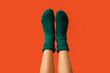 Legs of young woman in green knitted socks on orange background