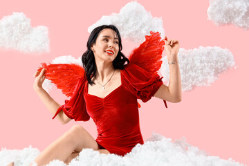 Obraz premium Beautiful young happy woman dressed as cupid sitting in clouds on pink background. Valentine's Day celebration