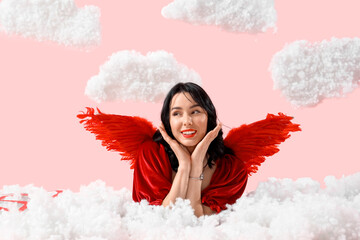 Obraz premium Beautiful young happy woman dressed as cupid lying in clouds on pink background. Valentine's Day celebration