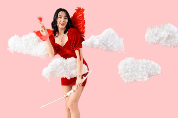 Obraz premium Beautiful young happy woman dressed as cupid with bow and arrow in clouds on pink background. Valentine's Day celebration